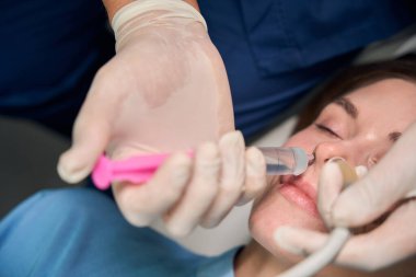 Doktorun hastaların burun bölgesini tedavi etmek için pembe bir tıbbi alet kullandığını gösteren detaylar.