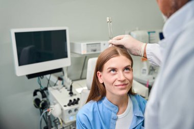 Doktor, hasta üzerinde işitsel tepkileri kontrol eden bir diyapazon işitme testi uygular.