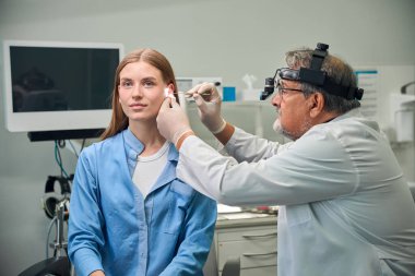 Farlı bir doktor, tıbbi bir işlem sırasında hastaların kulaklarını yakından inceler.