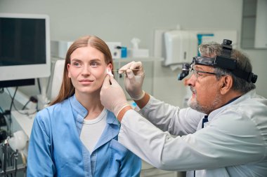 Doktor, klinik bir ortamda hastaların kulaklarını incelemek için tıbbi bir araç kullanıyor.