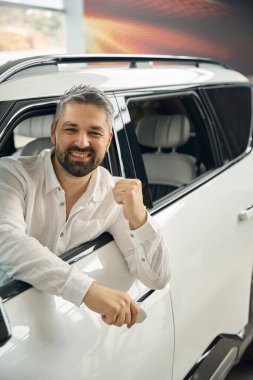 Kutlama yaparken yeni araba alan, pencereden dışarı bakan anahtarlı gülümseyen adam. Araba satışı, iş konsepti