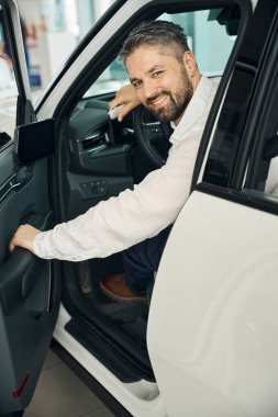 Mutlu yetişkin adam yeni bir araba alıyor, kameraya bakıyor. Araba satışı, iş konsepti