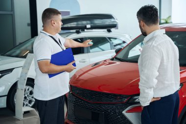 Satış müdürünün elinde dosya klasörü ve galeride duran adam. Araba satışı, iş konsepti