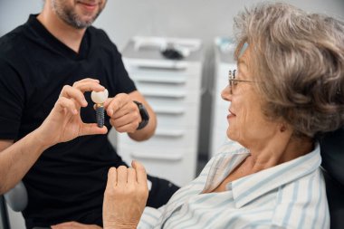 Hasta diş implantının modelini diş protezcisinin ellerinde inceler, doktor randevusunda ona danışır.