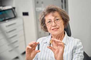 Randevudaki yaşlı kadın diş implantı bileşenlerinin modelini, dişçilikte modern teknolojilerin kullanımını inceliyor.