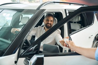 Araba galerisindeki satıcıdan araba anahtarı alan gülümseyen genç adam. Araba satışı, iş konsepti