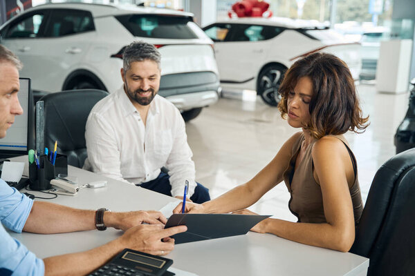 Девушка покупает новую машину в автосалоне и подписывает документы. Концепция страхования автомобиля