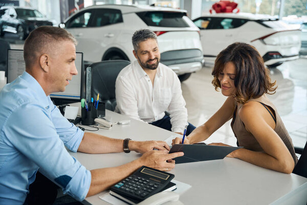 Молодая женщина покупает новую машину в автосалоне и подписывает документы. Концепция страхования автомобиля