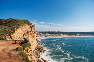 Güneş gözlüklü gülümseyen genç kadın Portekiz, Nazare 'nin güzel plajının tadını çıkarıyor. Seyahat, manzara konsepti
