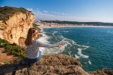 Güneş gözlüklü genç bir kadın, Portekiz 'deki Nazare plajının panoramik manzarasını seyrediyor. Seyahat, manzara konsepti