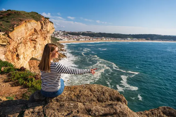 Güneş gözlüklü genç bir kadın, Portekiz 'deki Nazare plajının panoramik manzarasını seyrediyor. Seyahat, manzara konsepti