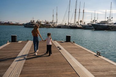 Mutlu genç anne ve kızı rıhtımda el ele yürüyorlar. Akdeniz 'deki Valencia Limanı, İspanya