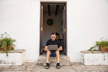 Güneş gözlüklü yetişkin bir adam Guadalest, İspanya 'daki binanın yakınlarında dizüstü bilgisayarla çalışıyor. Seyahat, mimari, yaşam tarzı konsepti