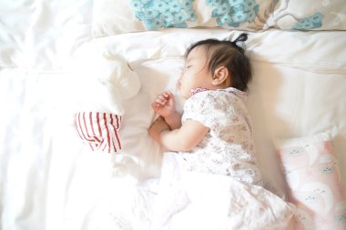 Cute sleepy 1 years old Asian infant girl sleeping on soft bedding with a doll, Newborn concept.