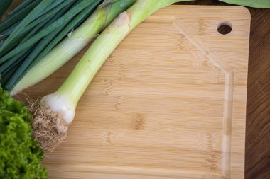 Pırasa, marul ve soğan kesme tahtasında. Yenilebilir sebzeler. Yemek ve gastronomi için gerekli malzemeler. Sağlıklı beslenme. Aşçılık faaliyetlerinde kullanılan yeşil baharatlar ve salatalar.