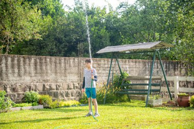 Brezilyalı çocuk bahçede su hortumuyla oynuyor..