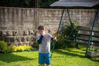Brezilyalı çocuk bahçede su hortumuyla oynuyor..