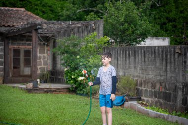 Brezilyalı çocuk bahçede su hortumuyla oynuyor..