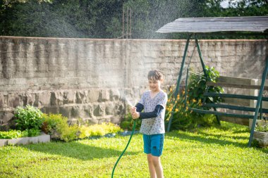 Brezilyalı çocuk bahçede su hortumuyla oynuyor..