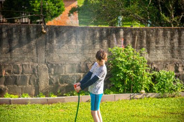 Brezilyalı çocuk güneşli bir öğleden sonra arka bahçesinde su hortumuyla oynuyor. Beyaz, beyaz, latin çocuk suyla oynuyor. Eğlenceliydi. Mutlu bir çocukluk. Arka bahçede oyun günü..
