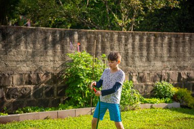 Brezilyalı çocuk güneşli bir öğleden sonra arka bahçesinde su hortumuyla oynuyor. Beyaz, beyaz, latin çocuk suyla oynuyor. Eğlenceliydi. Mutlu bir çocukluk. Arka bahçede oyun günü..