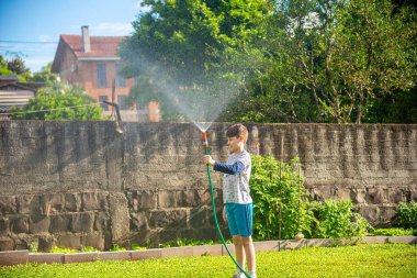 Brezilyalı çocuk güneşli bir öğleden sonra arka bahçesinde su hortumuyla oynuyor. Beyaz, beyaz, latin çocuk suyla oynuyor. Eğlenceliydi. Mutlu bir çocukluk. Arka bahçede oyun günü..