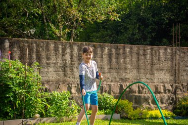 Brezilyalı çocuk güneşli bir öğleden sonra arka bahçesinde su hortumuyla oynuyor. Beyaz, beyaz, latin çocuk suyla oynuyor. Eğlenceliydi. Mutlu bir çocukluk. Arka bahçede oyun günü..