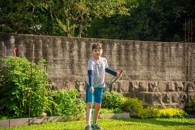 Brezilyalı çocuk güneşli bir öğleden sonra arka bahçesinde su hortumuyla oynuyor. Beyaz, beyaz, latin çocuk suyla oynuyor. Eğlenceliydi. Mutlu bir çocukluk. Arka bahçede oyun günü..