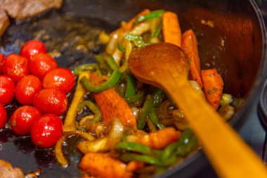 Biftek, soğanlı, domatesli ve biberli. Gaz ocağında kızartma tavasında hazırlanıyor.