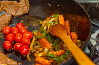 Biftek, soğanlı, domatesli ve biberli. Gaz ocağında kızartma tavasında hazırlanıyor.