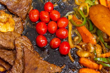 Biftek, soğanlı, domatesli ve biberli. Gaz ocağında kızartma tavasında hazırlanıyor.