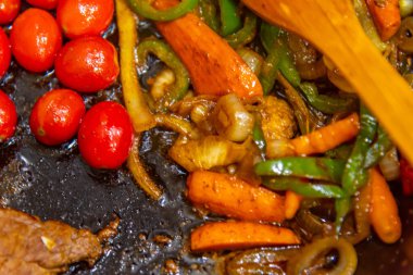 Biftek, soğanlı, domatesli ve biberli. Gaz ocağında kızartma tavasında hazırlanıyor.