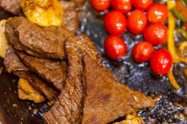 Biftek, soğanlı, domatesli ve biberli. Gaz ocağında kızartma tavasında hazırlanıyor.