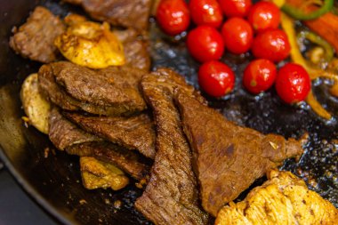 steak with onions, tomatoes and peppers being prepared in a frying pan on a gas stove clipart