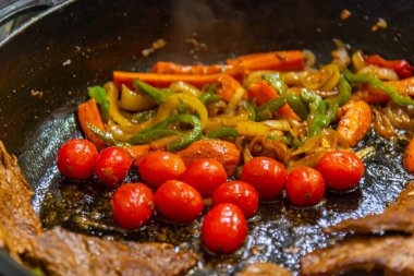 Biftek, soğanlı, domatesli ve biberli. Gaz ocağında kızartma tavasında hazırlanıyor.