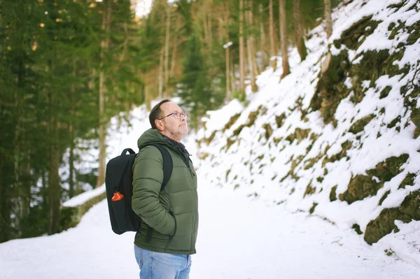 stock image Outdoor portrait of middle age 55 - 60 year old man hiking in winter forest, wearing warm jacket and black backpack