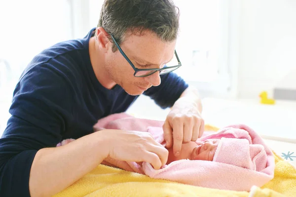 Father taking care of newborn baby, drying kid with towel after bathtime