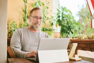 Portrait of middle age man working from home, using portable computer and mobile phone