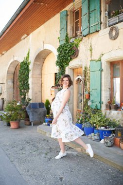 Outdoor portrait of happy young pregnant woman dancing on the street in countryside