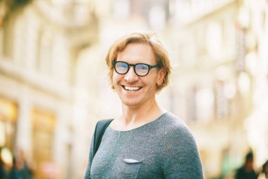 Outdoor portrait of handsome red-haired man wearing eyeglasses posing on city street
