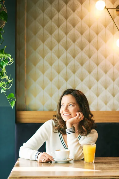 Portrait of happy healthy woman having coffee and orange juice in cafe