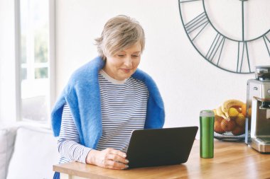 Evde dizüstü bilgisayarla çalışan mutlu orta yaşlı bir kadının portresi.