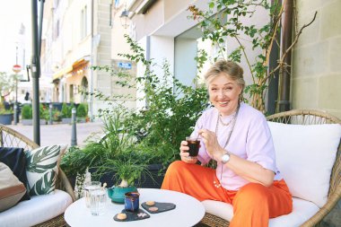 Açık hava kafesinde buzlu kahve içen mutlu olgun bir kadının portresi.