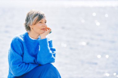 Güzel olgun bir kadının açık hava portresi. Göl ve denizin yanında dinleniyor. Uyarı sıcacık kazak giyiyor.