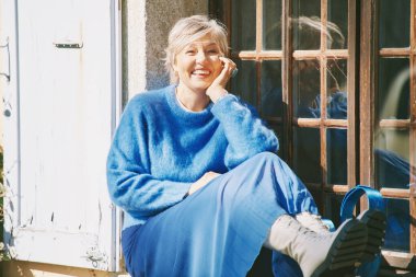 Pencerenin yanında oturan mutlu orta yaşlı kadının açık hava portresi.