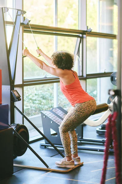 Mature woman exercising on machine at gym for arm and shoulders muscles