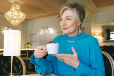 Zarif yaşlıların portresi 55 - 60 yaşında bir kadın rahat bir kafede kahve içiyor.