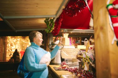 Açık hava portresi. Gri saçlı güzel orta yaşlı bir kadın. Noel alışverişinde hediyeler ve hediyeler alıyor.