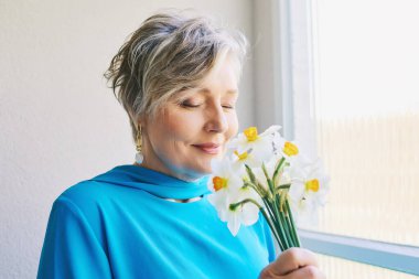 55-60 yaşlarında nergis çiçekli güzel bir kadının bahar portresi.