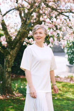 55-60 yaşındaki güzel bir kadının manolya ağacıyla poz verdiği bahar portresi.